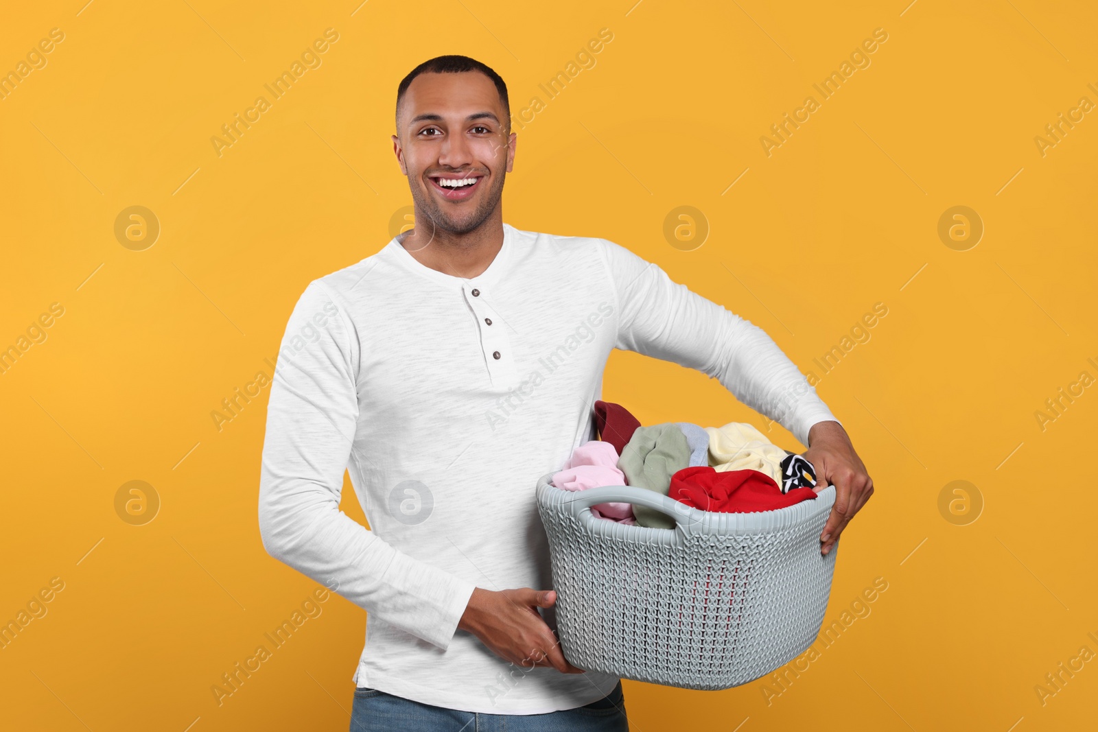 Photo of Happy man with basket full of laundry on orange background