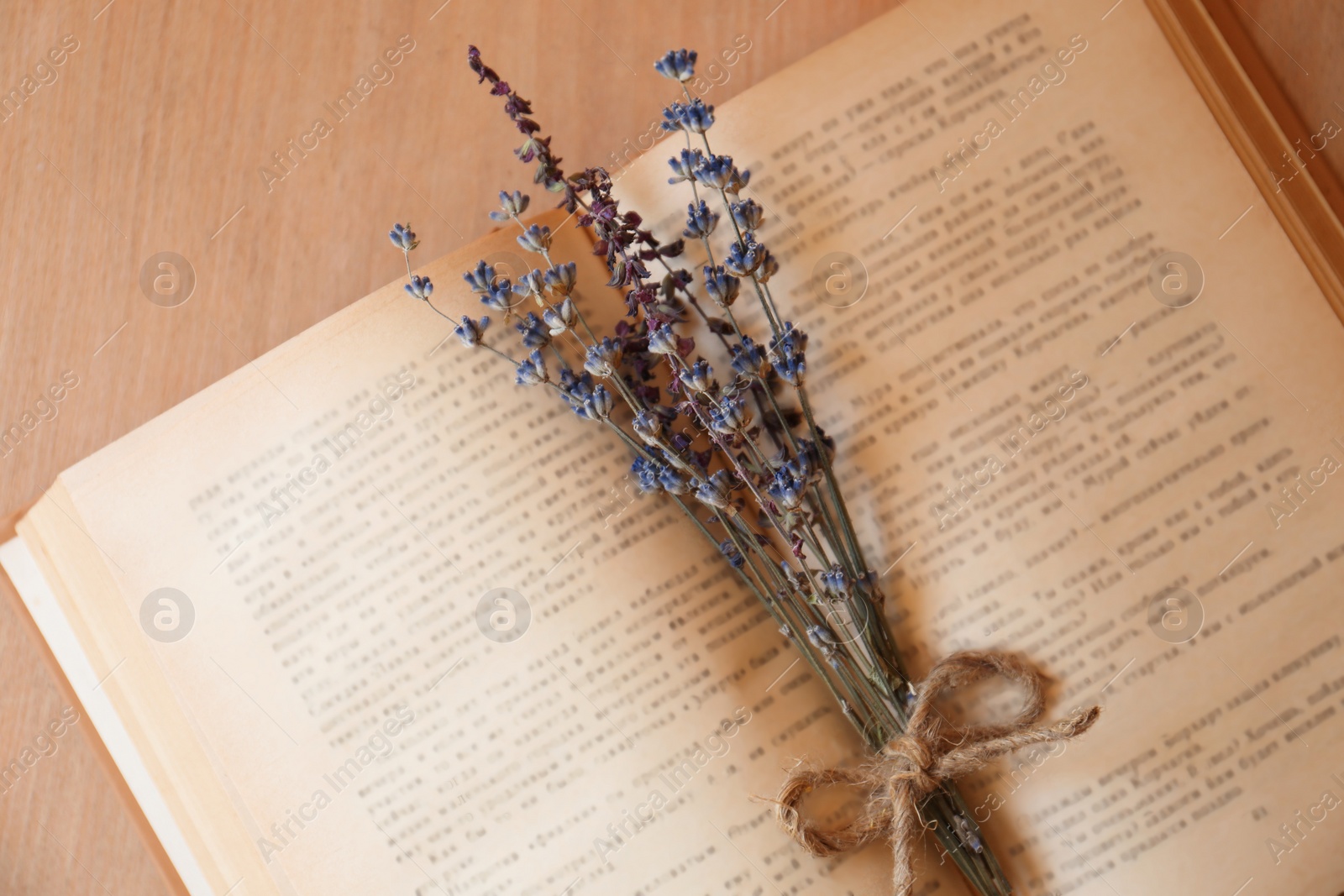 Photo of Open book with bunch of dried flowers on wooden table, closeup