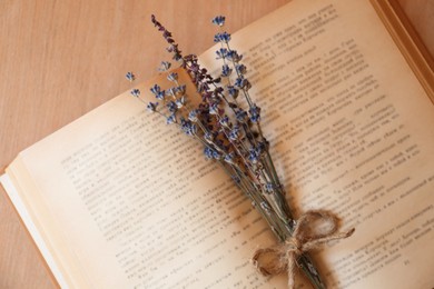 Photo of Open book with bunch of dried flowers on wooden table, closeup