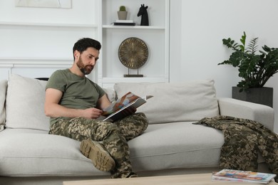 Photo of Soldier reading magazine on sofa in living room. Military service