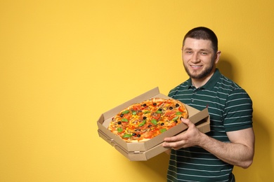 Photo of Attractive young man with delicious pizza on color background