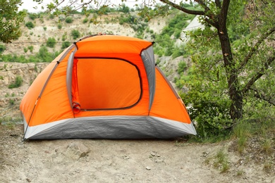 Modern camping tent near tree in wilderness