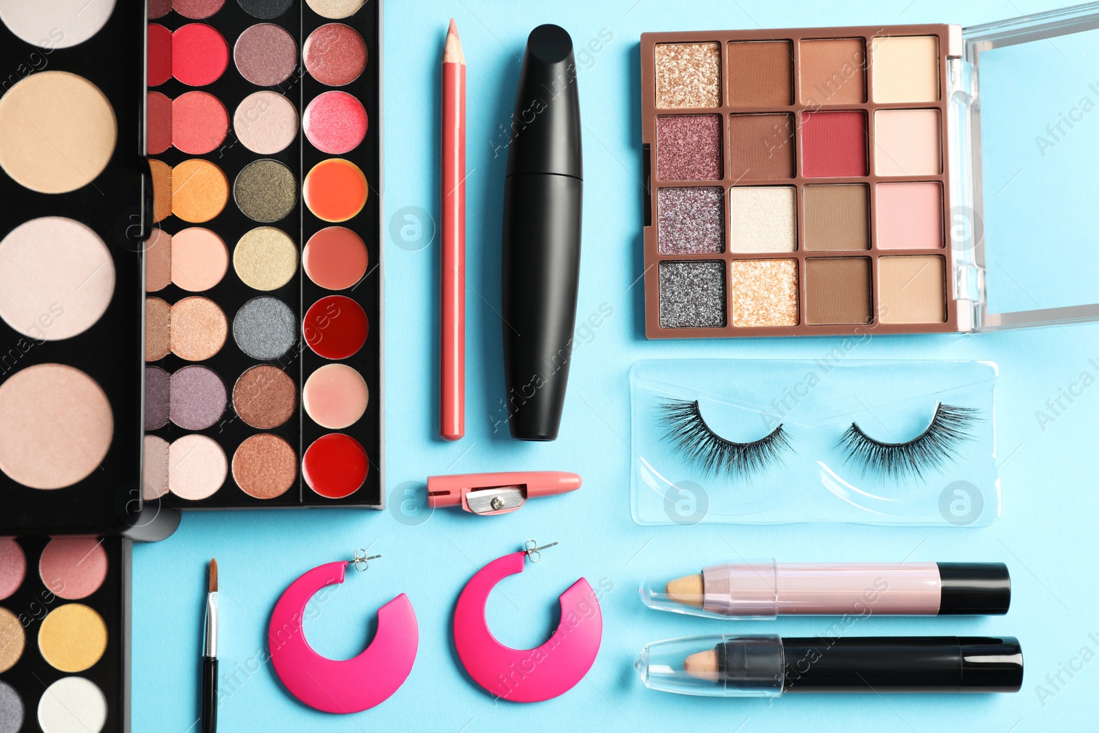 Photo of Set of makeup products and earrings on light blue background, flat lay