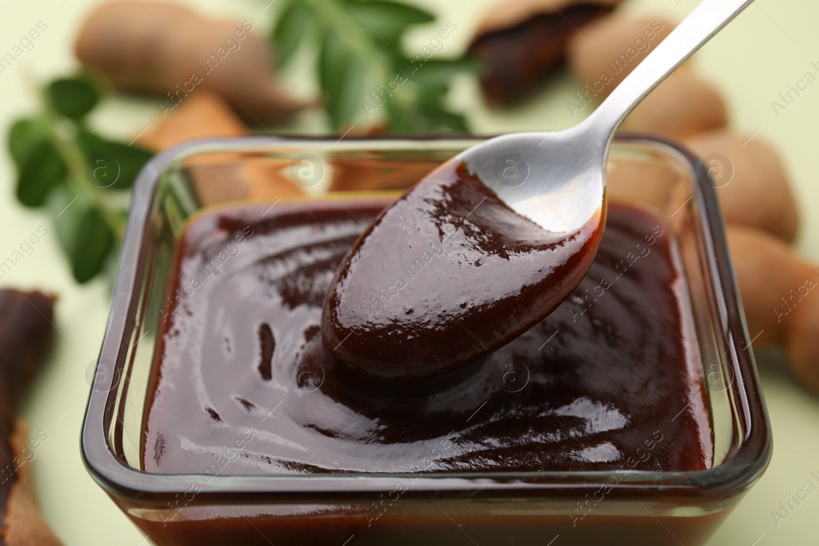 Taking tasty tamarind sauce with spoon from bowl on table, closeup Photo of Taking tasty tamarind sauce with spoon from bowl on table, closeup