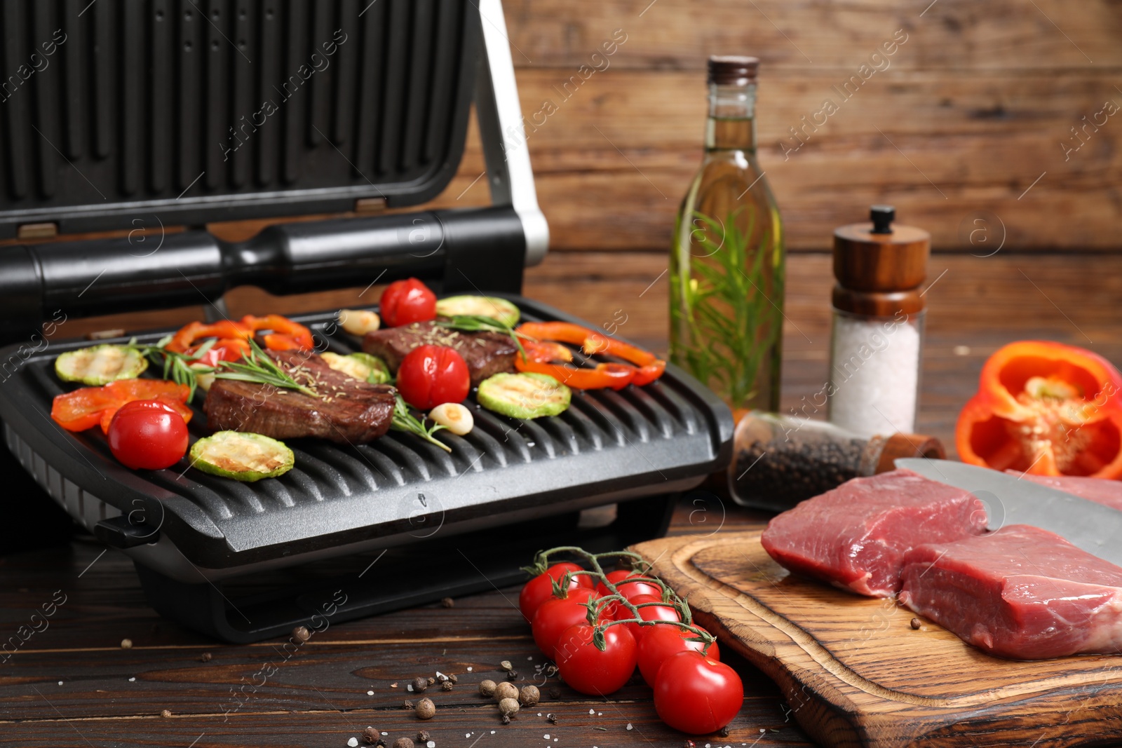 Photo of Electric grill with meat, spices and vegetables on wooden table