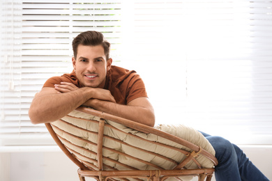 Photo of Attractive man relaxing in papasan chair near window at home