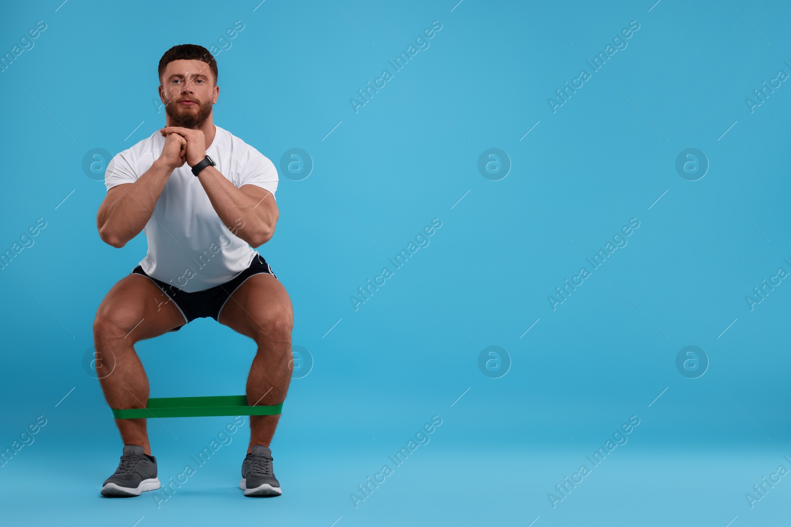 Photo of Young man exercising with elastic resistance band on light blue background. Space for text