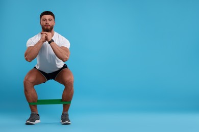 Young man exercising with elastic resistance band on light blue background. Space for text