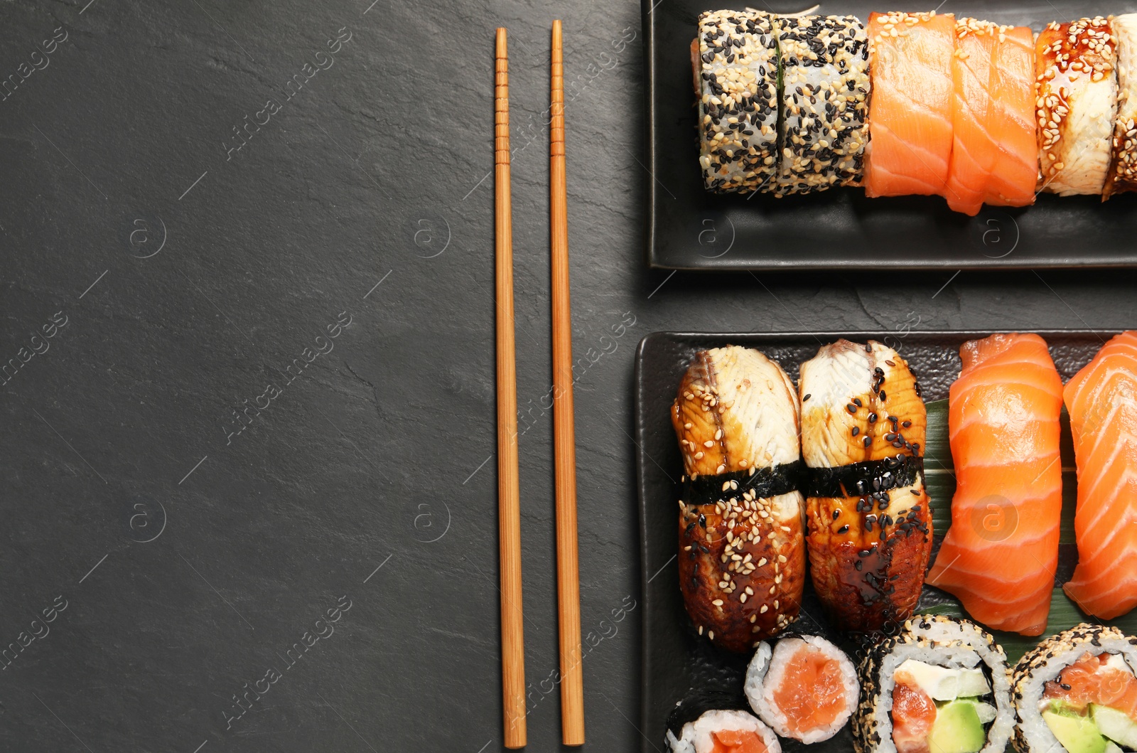 Photo of Delicious sushi rolls and chopsticks on black table, flat lay. Space for text