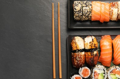 Photo of Delicious sushi rolls and chopsticks on black table, flat lay. Space for text