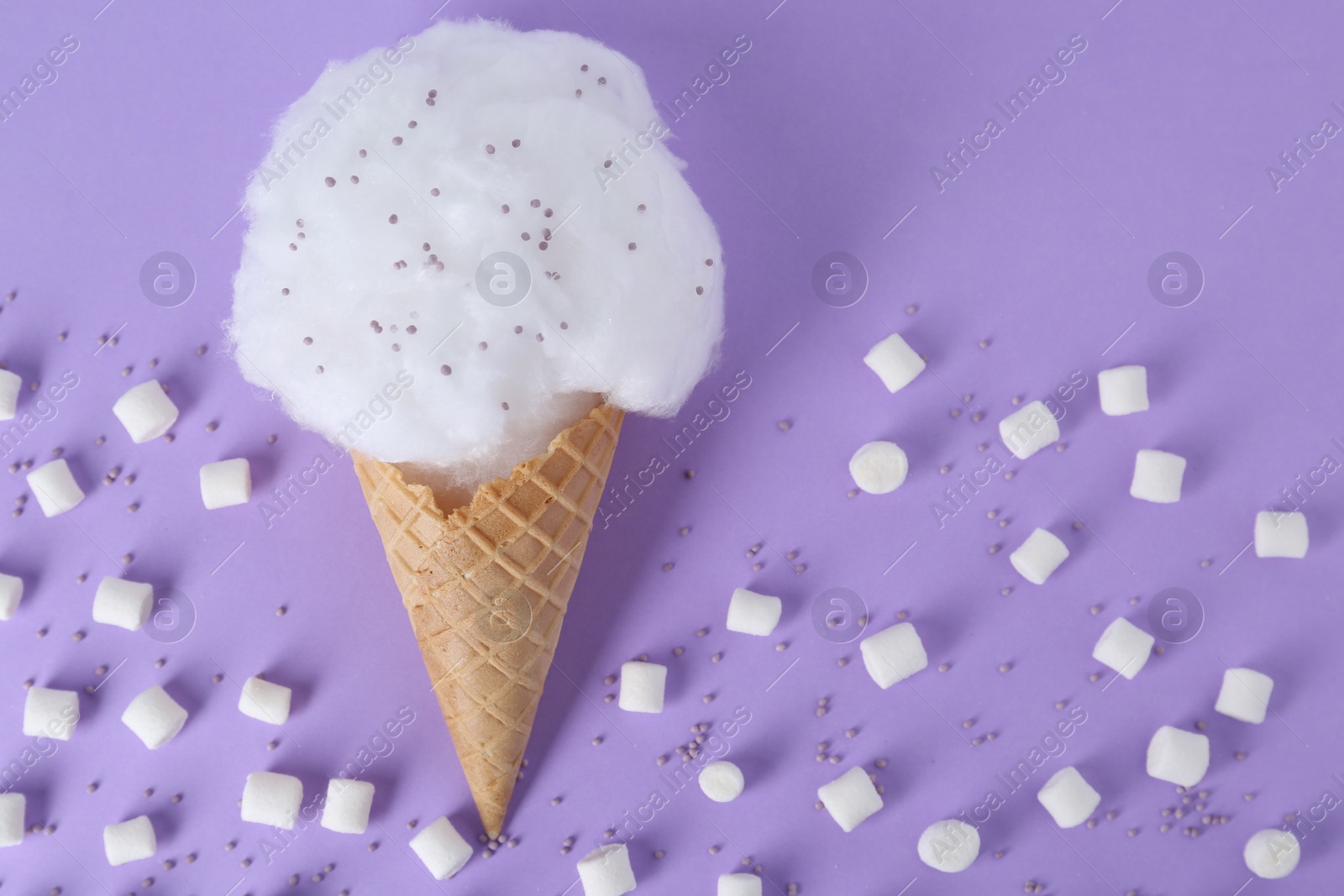 Photo of Sweet cotton candy in waffle cone and marshmallows on purple background, flat lay