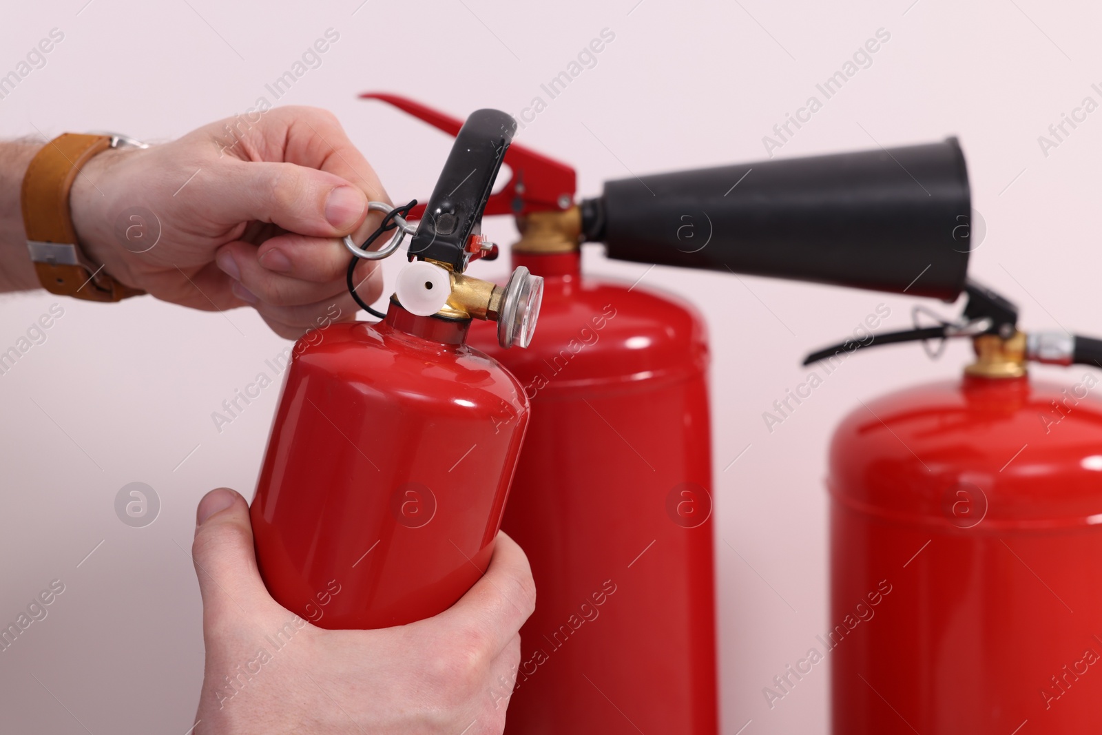 Photo of Man checking quality of fire extinguishers indoors, closeup