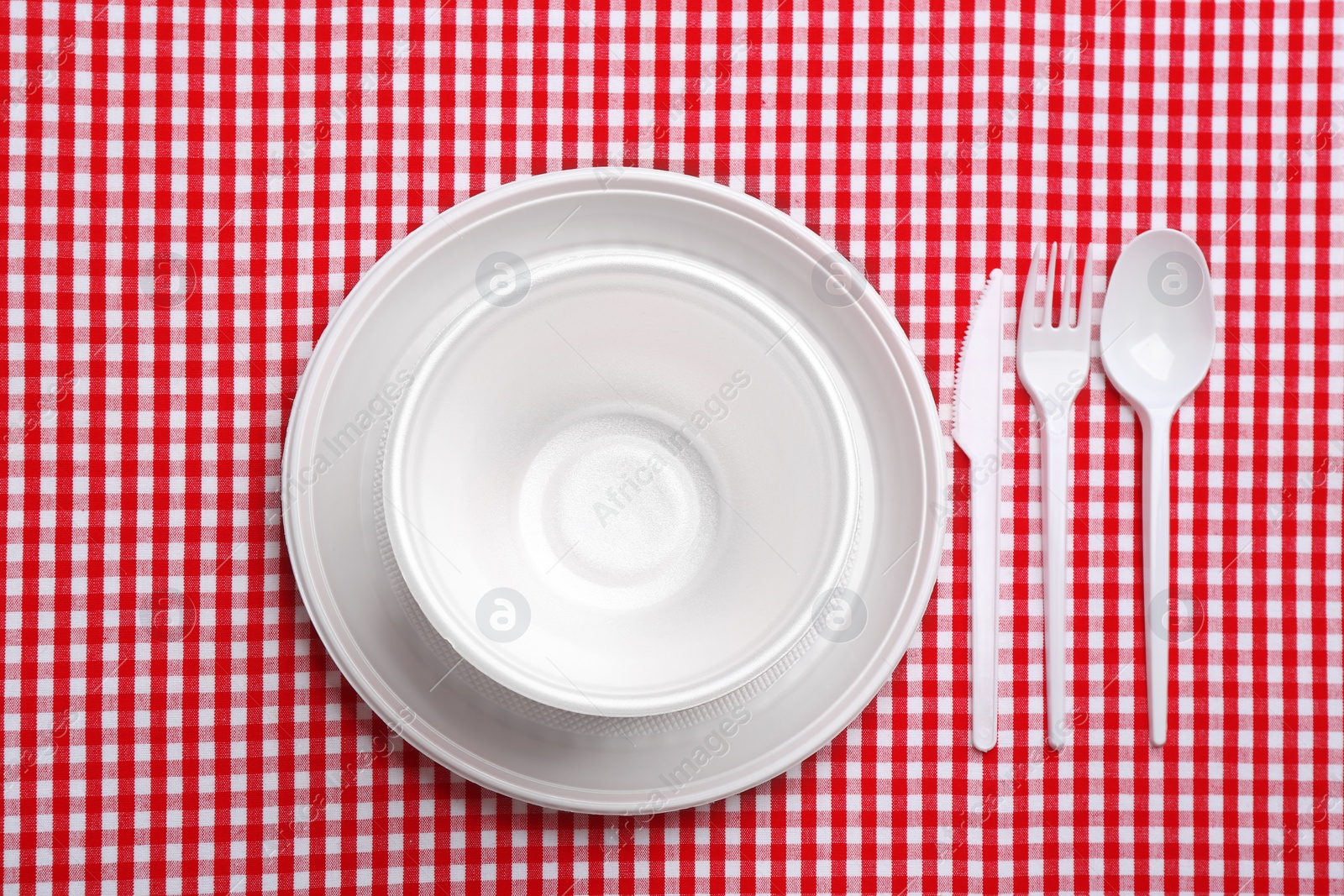 Photo of Table setting with plastic dishware on plaid fabric, flat lay