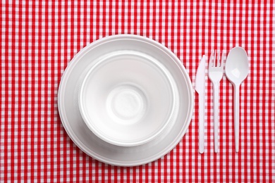 Table setting with plastic dishware on plaid fabric, flat lay