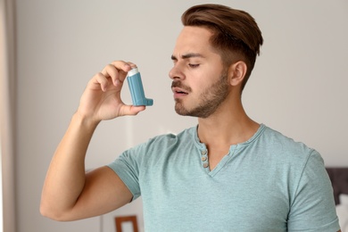 Young man using asthma inhaler at home