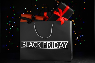 Paper shopping bag with gift boxes against blurred lights. Black Friday sale