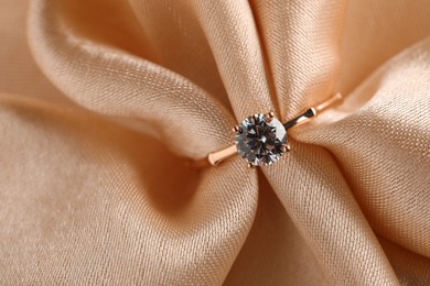 Beautiful engagement ring with gemstone on beige fabric, top view