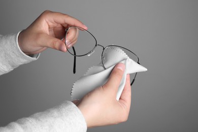 Photo of Woman cleaning glasses with microfiber cloth on light gray background, closeup