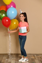 Happy girl with birthday gift and balloons on brown background