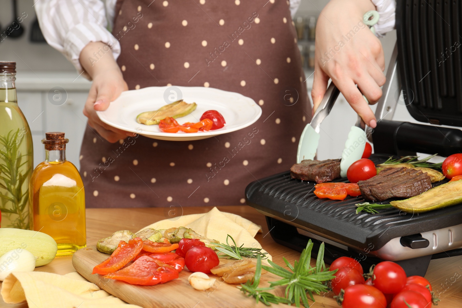 Photo of Woman cooking different products with electric grill at wooden table in kitchen, closeup