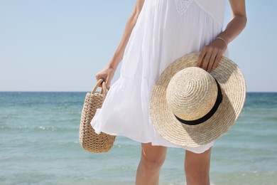 Photo of Woman with beach bag and straw hat near sea, closeup