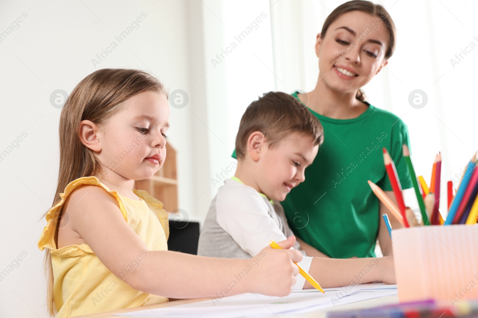 Photo of Little children with kindergarten teacher drawing at table indoors. Learning and playing