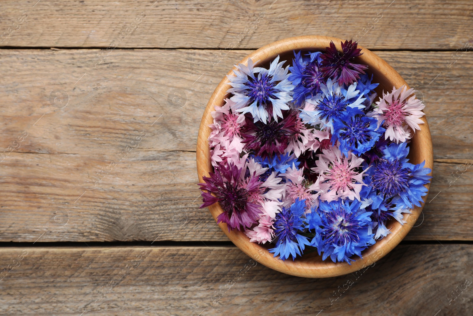 Photo of Beautiful colorful cornflowers in bowl on wooden table, top view. Space for text