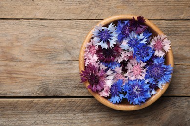 Beautiful colorful cornflowers in bowl on wooden table, top view. Space for text