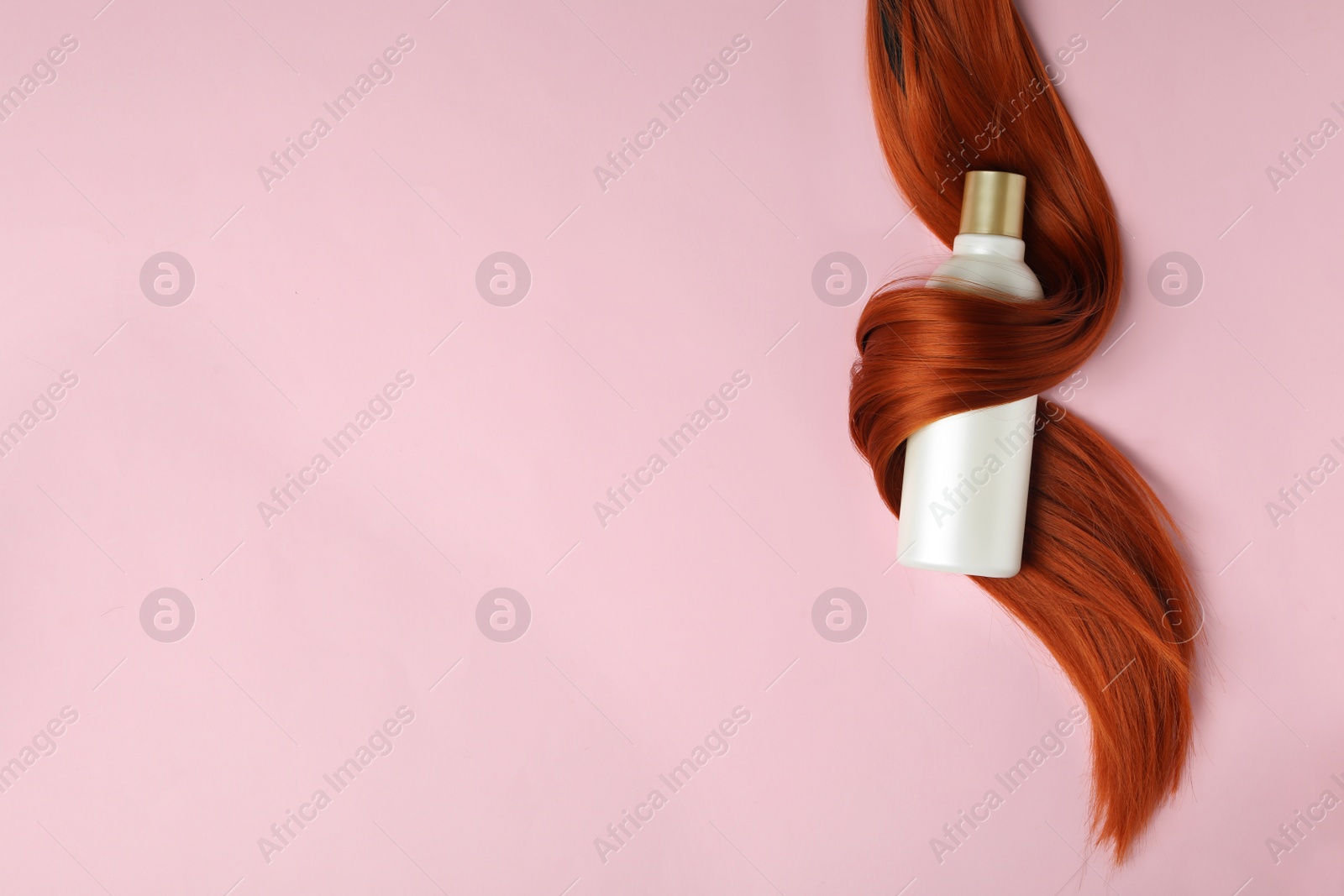 Photo of Shampoo bottle wrapped in lock of hair on pink background, flat lay with space for text. Natural cosmetic products