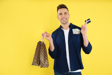 Happy man with cash money, shopping bags and credit card on yellow background
