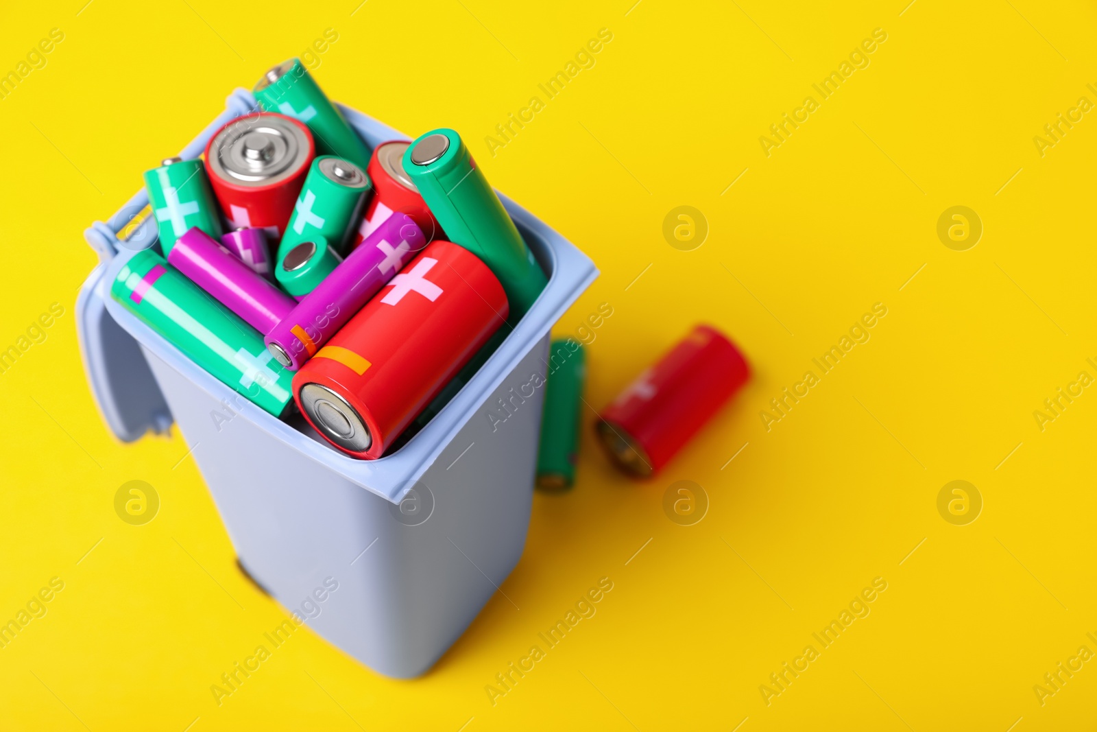 Photo of Many used batteries in recycling bin on yellow background, closeup. Space for text