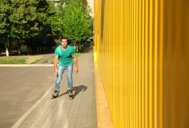 Handsome young man roller skating near yellow building, space for text