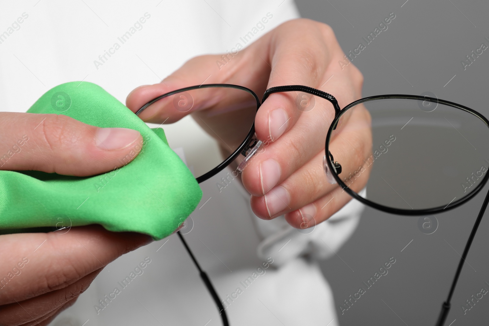 Photo of Woman wiping her glasses with microfiber cloth on grey background, closeup