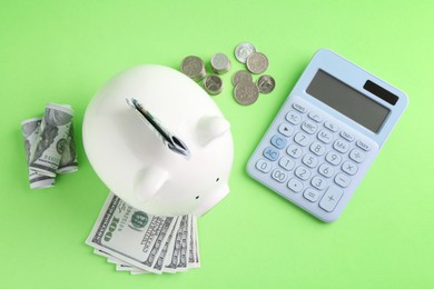 Photo of Financial savings. Piggy bank, dollar banknotes, coins and calculator on green background, flat lay