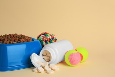 Bottle with vitamins, toys and dry pet food in bowl on beige background, space for text