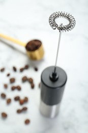 Photo of Black milk frother wand and coffee beans on white marble table