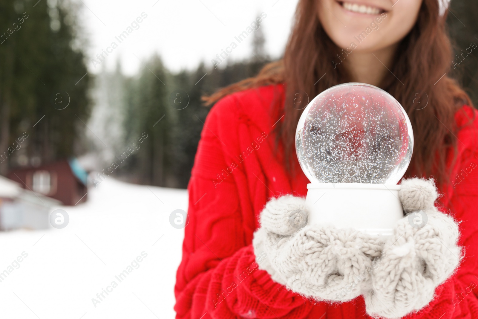 Photo of Woman with knitted mittens holding snow globe outdoors, closeup