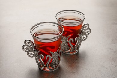 Photo of Glasses of traditional Turkish tea in vintage holders on light grey table, closeup