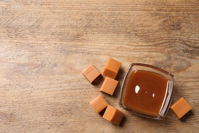 Tasty salted caramel in glass bowl and candies on wooden table, flat lay. Space for text