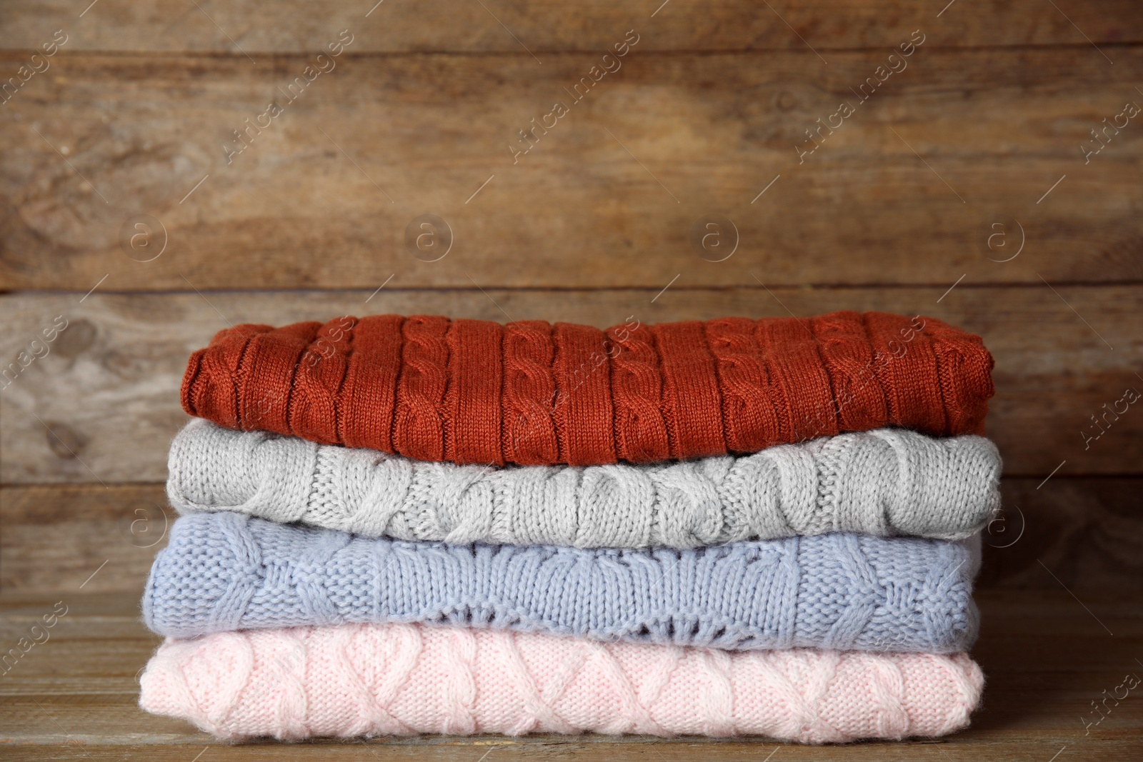 Photo of Stack of sweaters on wooden background. Autumn clothes