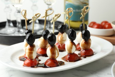 Photo of Tasty canapes with black olives, mozzarella and cherry tomatoes on white marble table, closeup