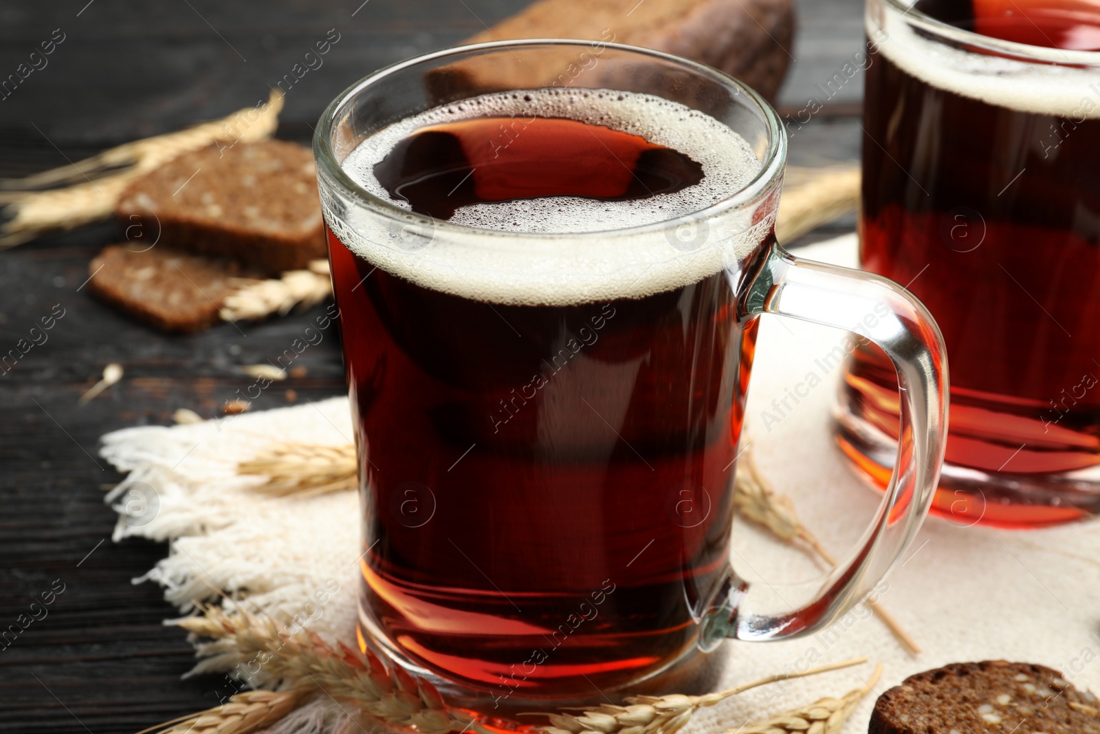 Photo of Mugs of delicious kvass, spikes and bread on table