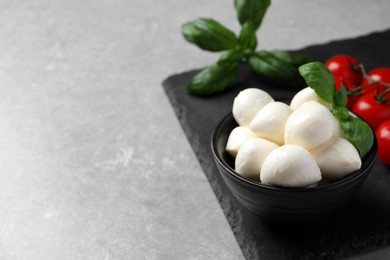 Photo of Delicious mozzarella balls, basil and tomatoes on light gray table, space for text
