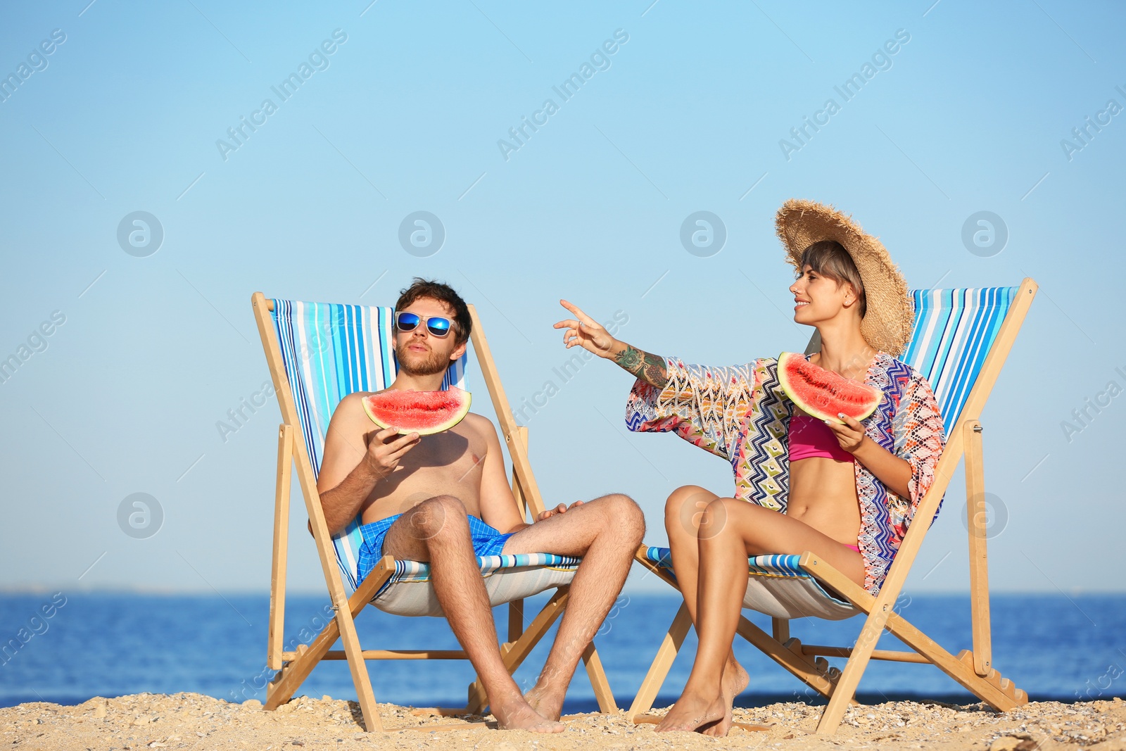 Photo of Young couple with watermelon slices in beach chairs at seacoast