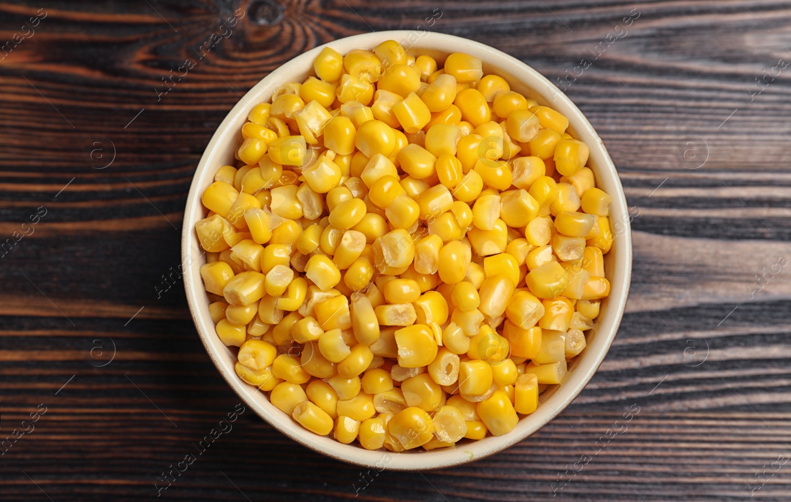 Photo of Delicious canned corn in bowl on wooden table, top view