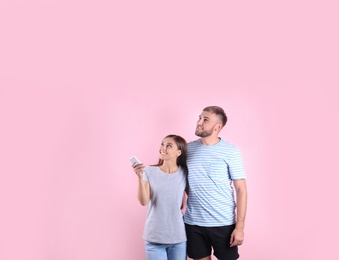 Young couple with air conditioner remote on color background