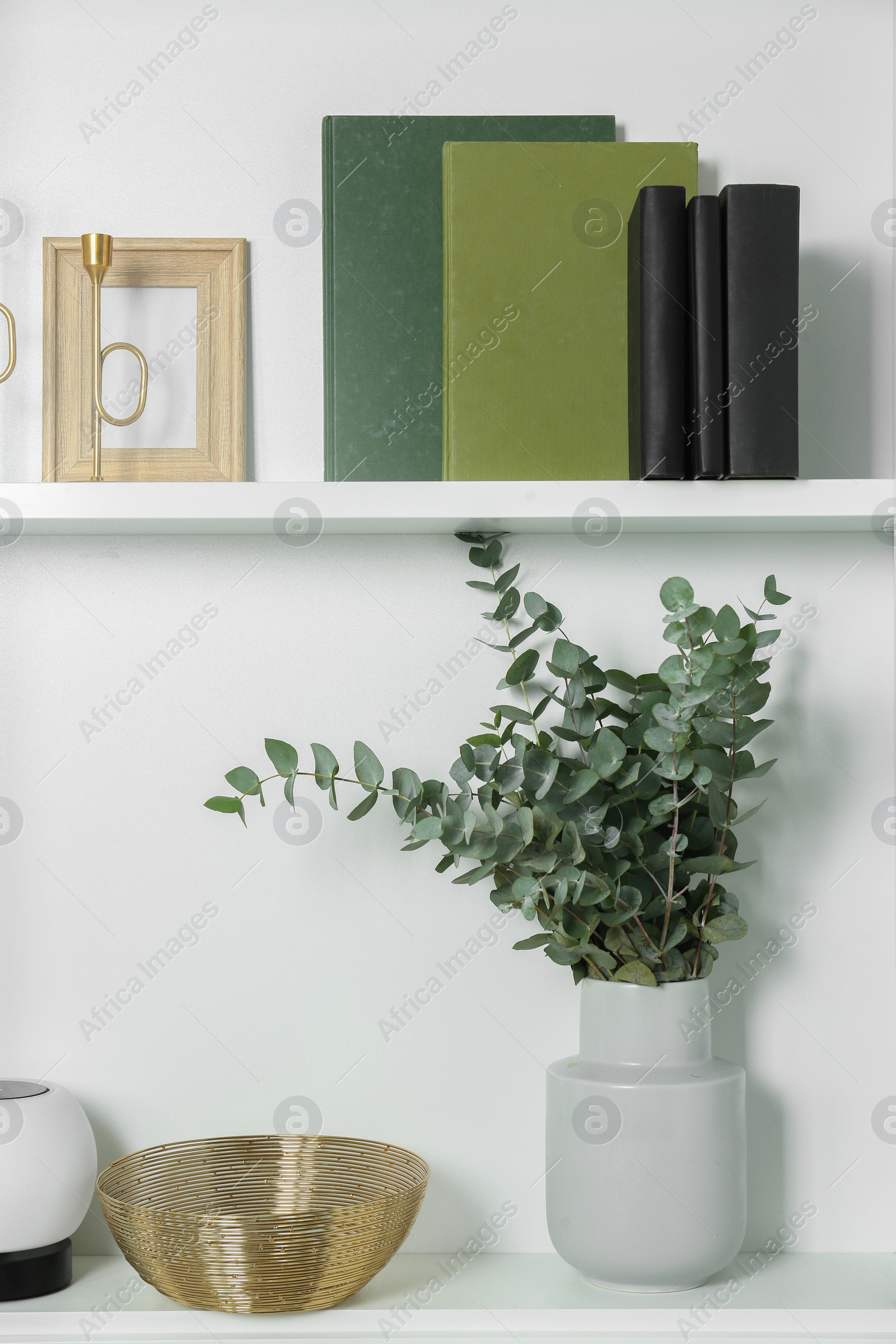 Photo of White shelves with books, eucalyptus and different decor indoors. Interior design