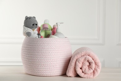 Photo of Basket with different baby cosmetic products, towel and toy on white wooden table