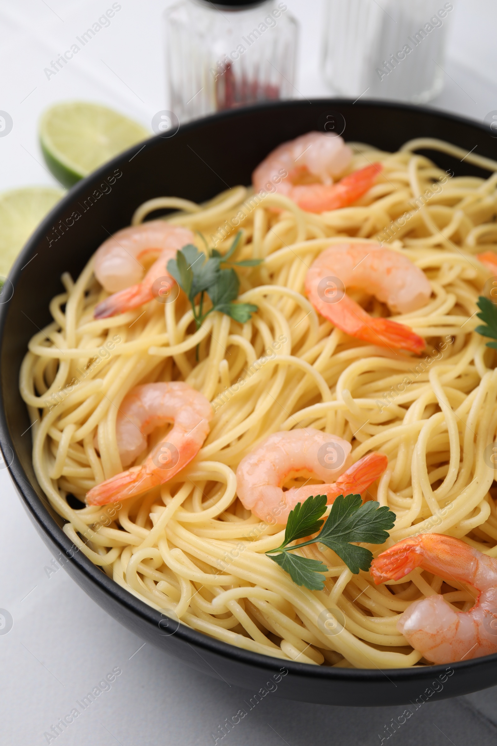 Photo of Tasty spaghetti with shrimps and parsley in bowl on light tiled table, closeup