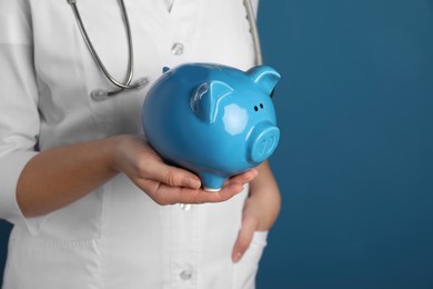 Photo of Doctor holding piggy bank on blue background, closeup. Space for text. Medical insurance